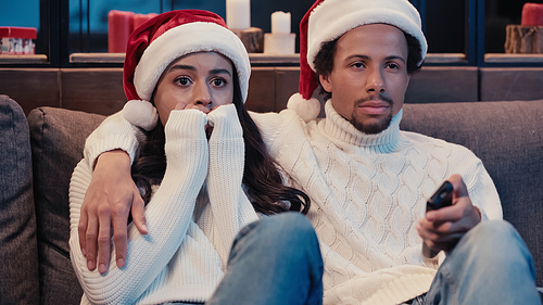African american man watching movie with scared girlfriend in santa hat
