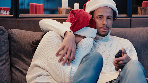 African american man watching film with scared girlfriend in santa hat