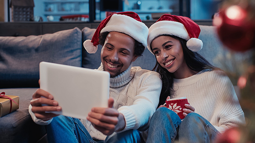 happy african american man near woman looking at digital tablet near blurred christmas tree