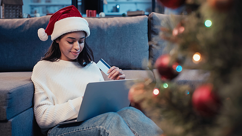 happy african american woman holding credit card and using laptop near christmas tree
