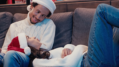 african american man in santa hat sticking out tongue near woman on cough
