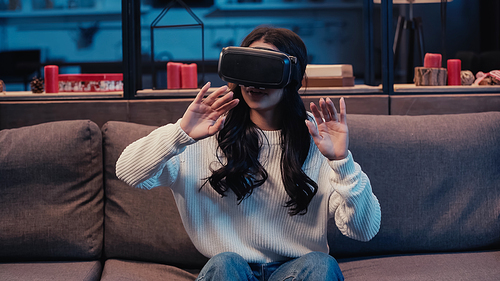 young african american woman in virtual reality headset gesturing while gaming at home