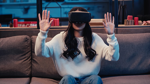brunette african american woman in virtual reality headset gesturing while gaming at home