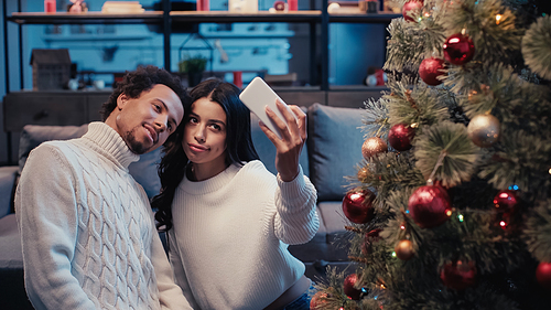 young african american couple taking selfie near christmas tree