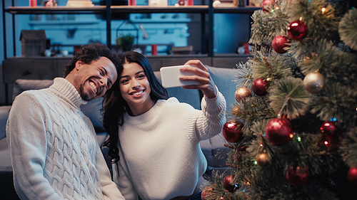 happy african american man taking selfie with woman near christmas tree