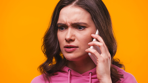 nervous woman in pink hoodie talking on mobile phone isolated on yellow