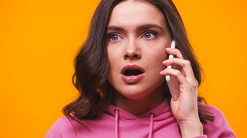shocked woman with open mouth calling on smartphone isolated on yellow