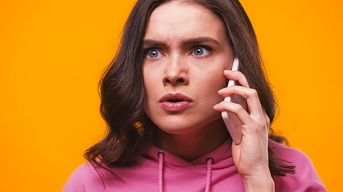angry woman in pink hoodie talking on smartphone isolated on yellow