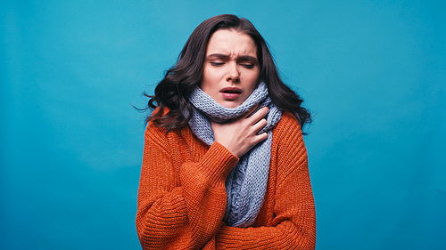 ill woman in warm scarf touching neck while suffering from pain in throat isolated on blue