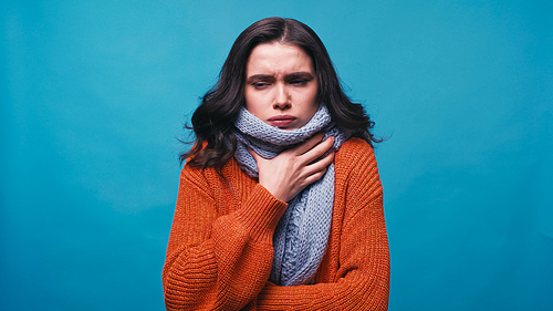 sick woman in warm scarf touching neck while suffering from pain in throat isolated on blue