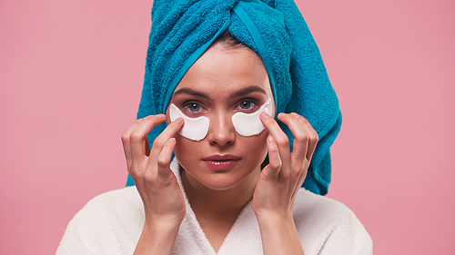 pretty woman with towel on head applying eye patches isolated on pink