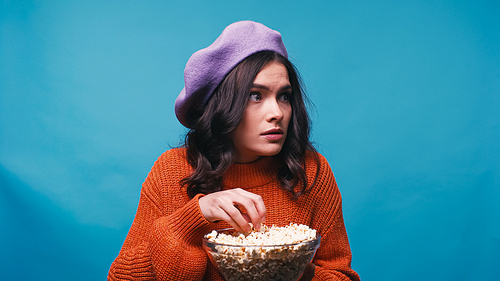frightened woman with bowl of popcorn watching movie isolated on blue