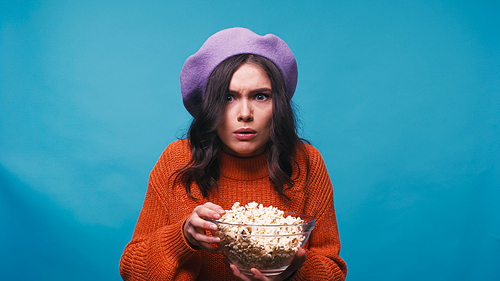 impressed woman with popcorn watching breathtaking movie isolated on blue