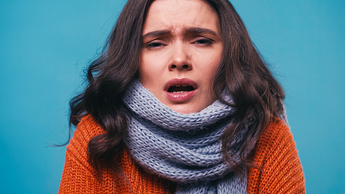 ill woman in knitted scarf sneezing while  isolated on blue