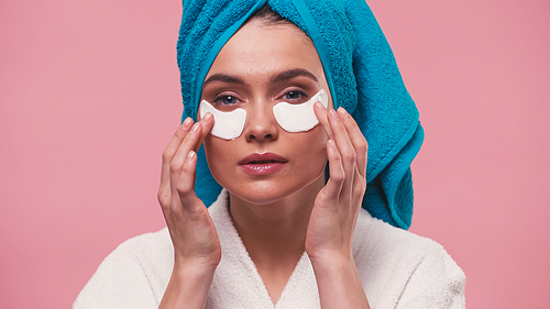 young woman  while applying eye patches isolated on pink