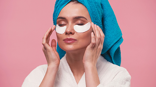 woman with closed eyes applying eye patches isolated on pink