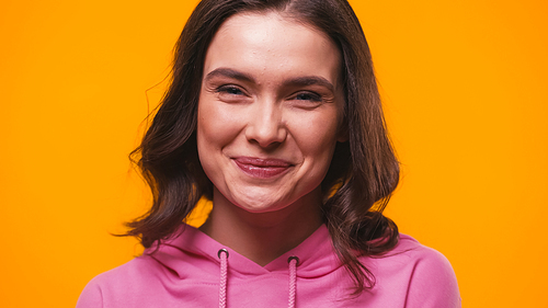 young brunette woman in pink hoodie smiling at camera isolated on yellow