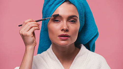 woman with towel on head styling eyebrows with eyebrow brush isolated on pink