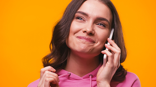 cheerful woman looking away while talking on smartphone isolated on yellow