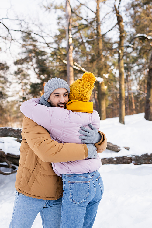 Smiling man hugging girlfriend in winter outfit in park at daytime