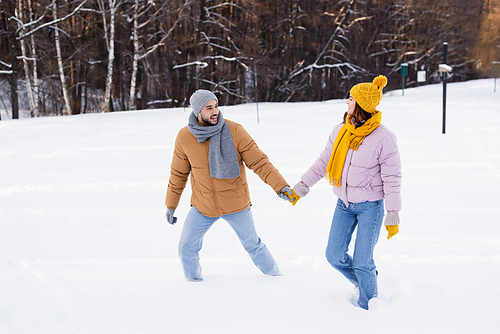 Smiling couple holding hands while walking on snow in park