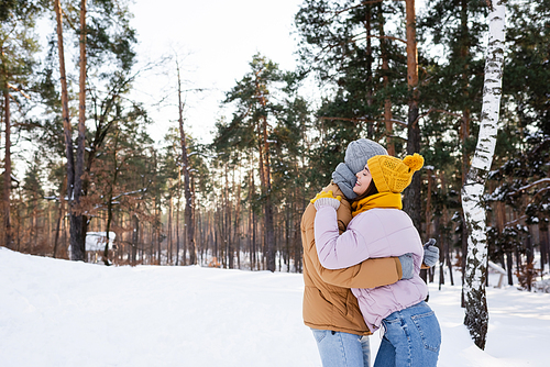 Side view of woman smiling and embracing boyfriend in winter park
