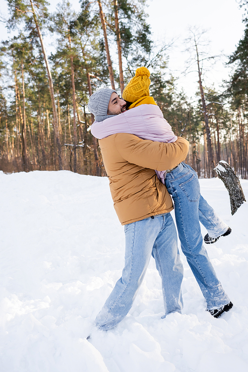 Happy man lifting girlfriend in snow in winter park