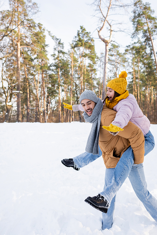 Excited woman piggybacking on boyfriend in winter park