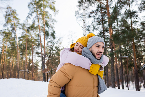 Woman with closed eyes embracing cheerful boyfriend in winter park
