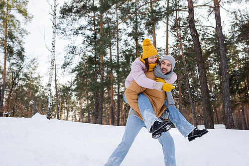 Happy woman piggybacking on boyfriend while having fun in winter park