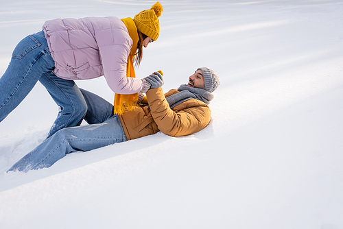 Positive couple in warm clothes playing on snow outdoors