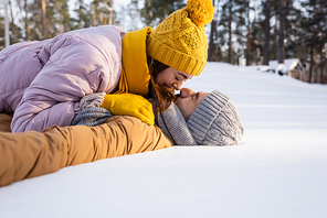 Side view of young couple in hats kissing while lying on snow