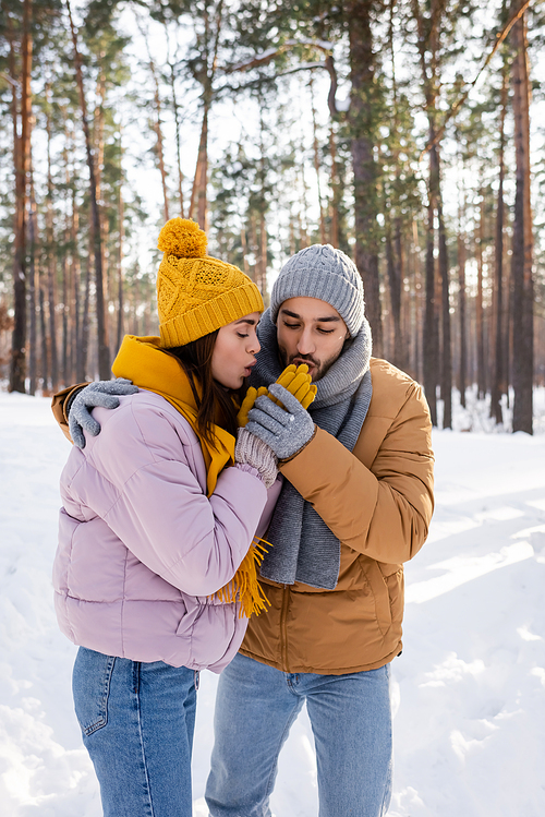 Young couple warming hands in gloves in winter park