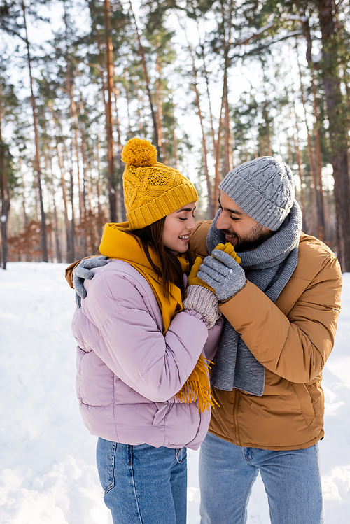 Smiling man hugging girlfriend and holding hands in winter park