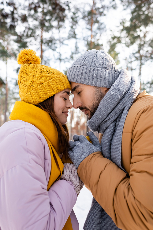 Side view of couple in knitted hats holding hands in winter park