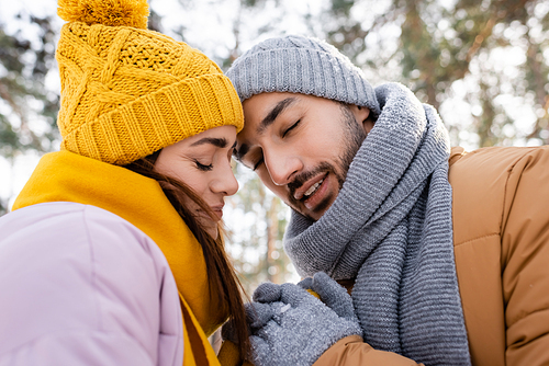 Smiling couple with closed eyes holding hands in winter park