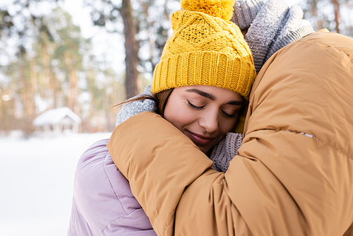 Man embracing young girlfriend in knitted hat in winter park