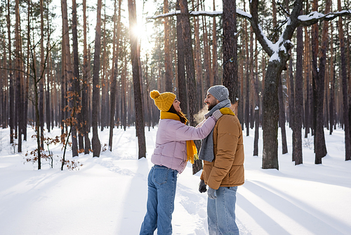 Side view of cheerful woman embracing boyfriend in snowy park