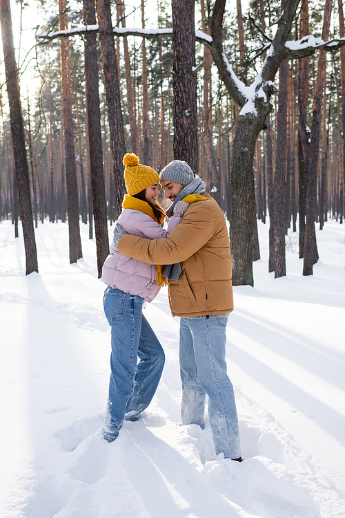 Side view of smiling couple in winter outfit embracing in snowy park