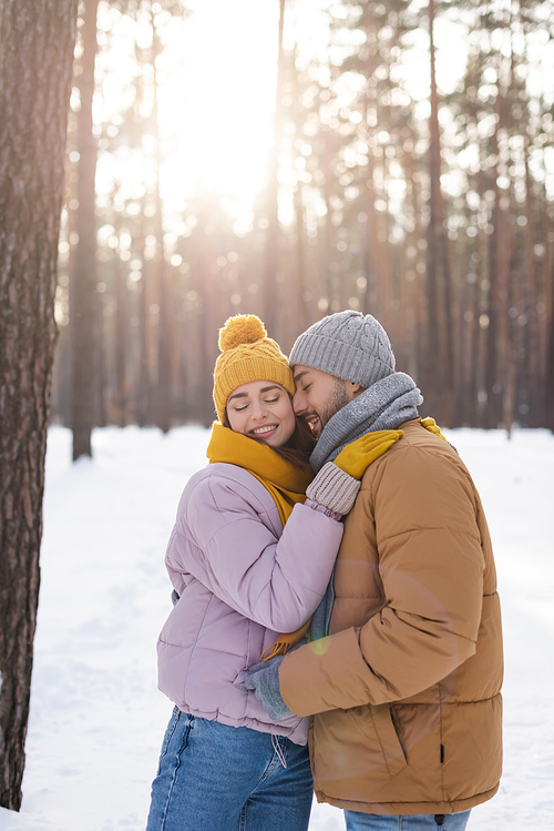 Smiling man with closed eyes standing near girlfriend in winter park