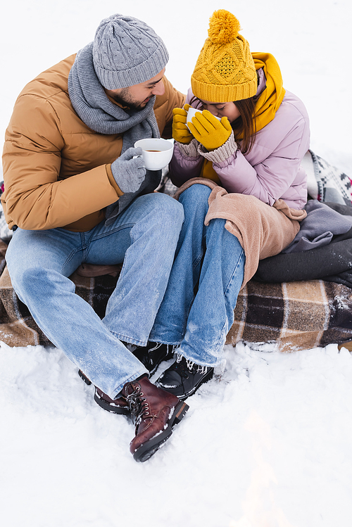 Young woman drinking coffee near boyfriend in snowy park