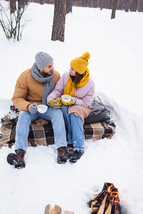 Couple with coffee cups holding hands near bonfire in snowy park