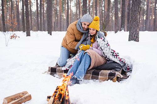 Man hugging girlfriend with cup near bonfire in winter park