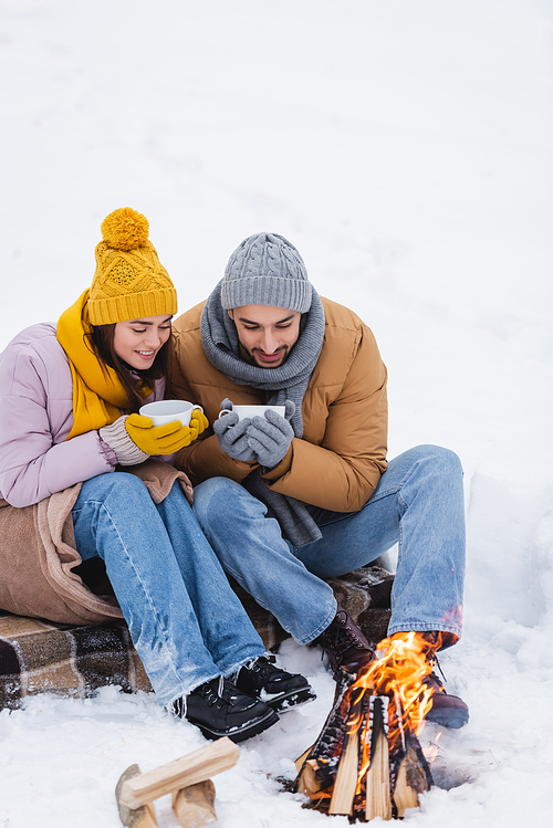 Couple with cups looking at bonfire on snow in park