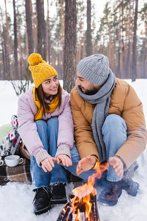Smiling couple warming hands near bonfire in winter park