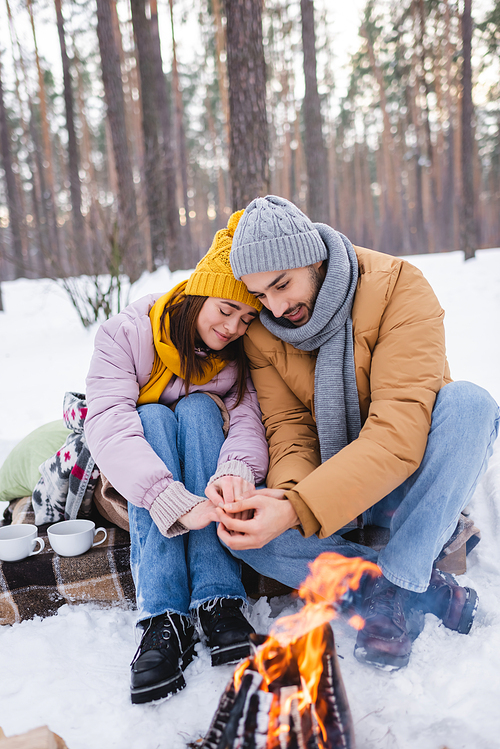 Young couple in winter outfit warning hands near bonfire in park