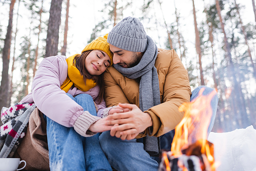 Young couple holding hands near bonfire in winter park