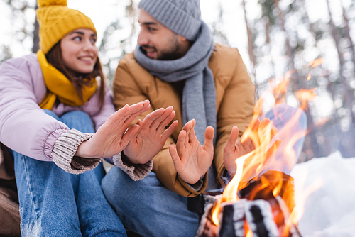 Bonfire near blurred couple warming hands in winter park