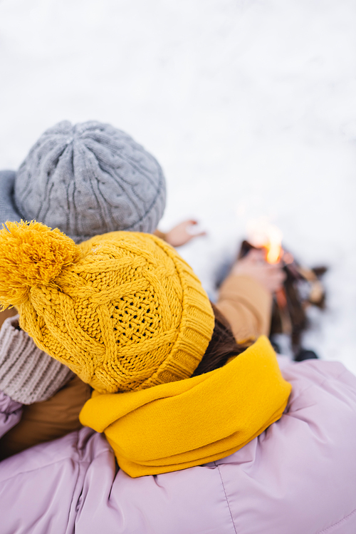 Overhead view of couple in knitted hats near blurred bonfire in winter park