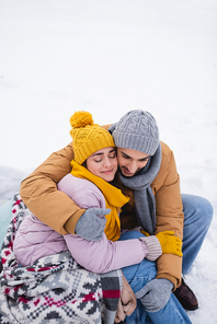 High angle view of smiling woman in blanket hugging boyfriend on snow in park
